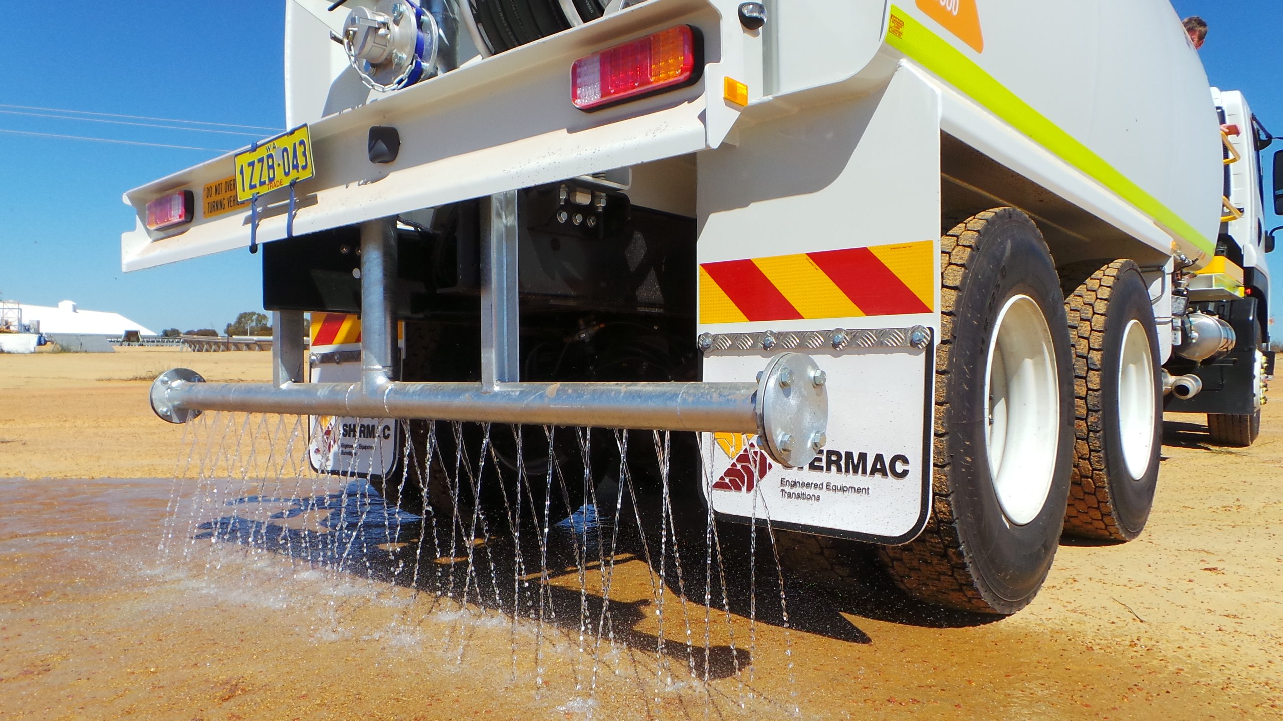 Shermac water cart truck actively spraying water from the horizontal spray bar onto a dusty mining