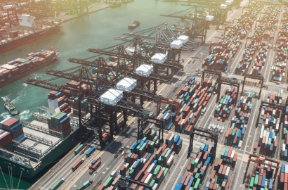 Global shipping port with container vessels and stacked freight containers illustrating supply chain disruptions and logistics delays.