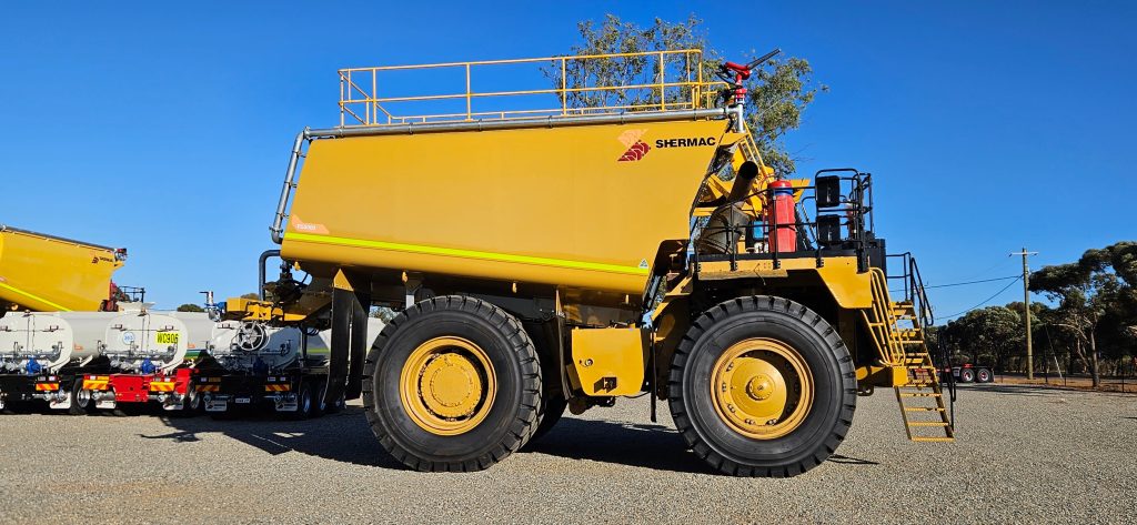 Side profile of a Shermac off-road water cart, other completed vehicles visible behind in WA