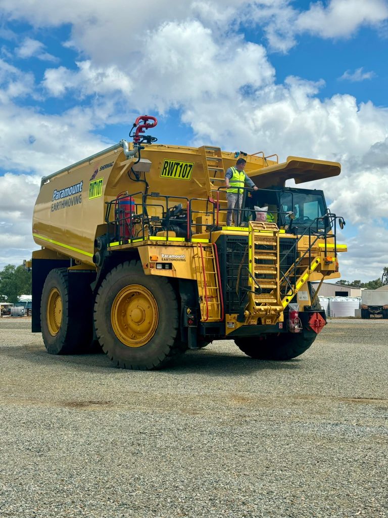 Low-angle view of a massive yellow mine-spec Shermac off-road water cart parked.