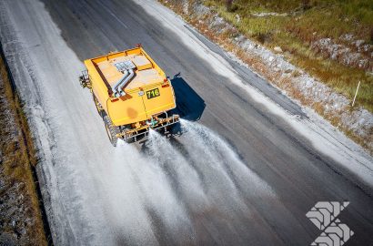 Rigid off-road water cart spraying haul road for dust suppression on a mining site, showing high-capacity tank and rear spray system in operation