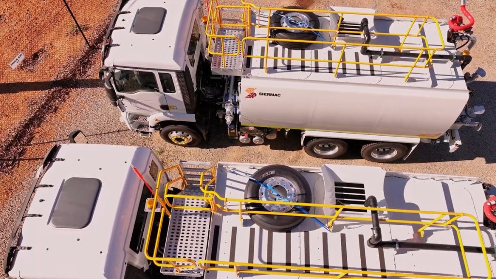 Overhead view of two white Shermac water trucks with yellow handrails parked at a site