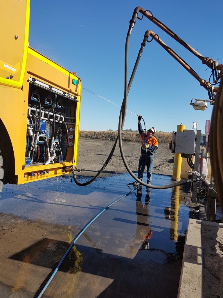 Mine-site operator handling a service truck hose during heavy equipment servicing.